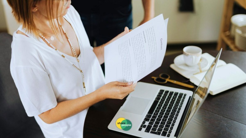 freelancer die bekijkt op papier hoe dekking van een verzekering is terwijl ze achter laptop zit.