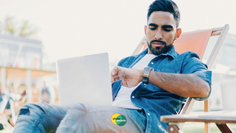 freelancer die op z'n horloge kijkt terwijl hij achter de laptop zit