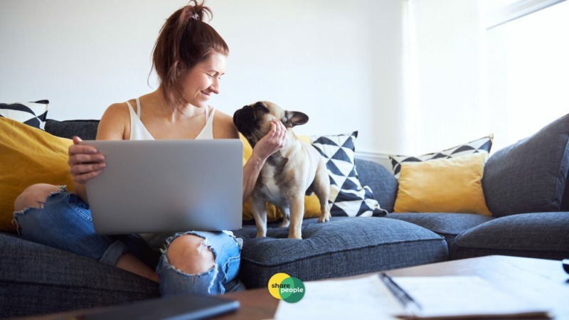 zzp'er op de bank met laptop die blij is en lacht naar haar hond