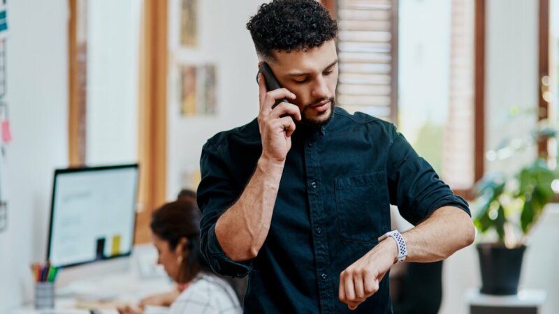 man die op horloge kijkt en aan de telefoon zit