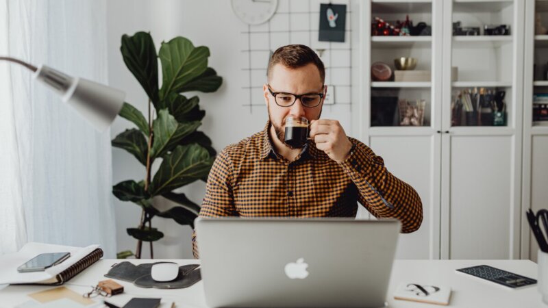 zzp'er drinkt kopje koffie achter zijn laptop en leest artikel over 8 manieren om financieel veilig te zitten.